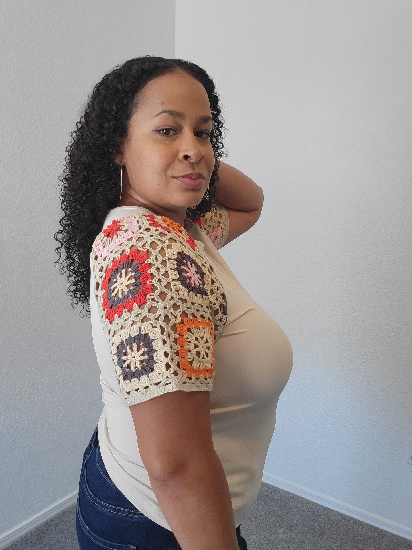 Woman wearing a colorful crochet sleeve fuller bust top on a plain background